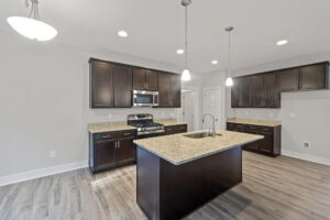 Modern kitchen with dark wood cabinetry, granite countertops, a center island with sink, stainless steel appliances, wood flooring, pendant lighting, and recessed ceiling lights.