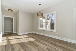 Empty modern living room with hardwood floors, large window, and a hanging light fixture.