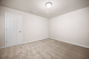 Empty room with beige walls and carpet, featuring a closed white door and a ceiling light.