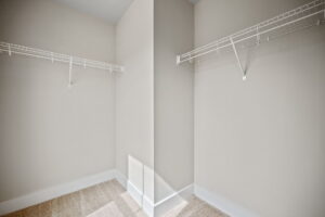 A walk-in closet with beige walls and carpet, featuring two white, metal wire shelves on either side.