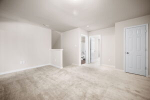 A carpeted room with beige walls, a small half-wall partition, two doors (one closed, one open leading to a bathroom), and recessed lighting.
