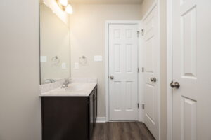 Modern bathroom with a dark vanity, large mirror, and two white doors on a light colored wall.
