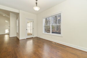 Empty living room with hardwood floors, a large window, and a white door leading outside. the walls are painted white and there is a ceiling light fixture.