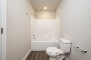 Minimalist bathroom with a white bathtub-shower combo, toilet, and wood-patterned floor.