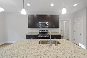 Modern kitchen with dark wood cabinets, stainless steel appliances, and granite countertops featuring a central island with an integrated sink and contemporary pendant lighting.