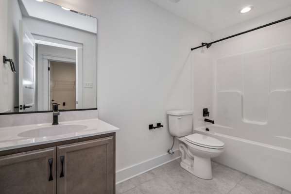 A modern bathroom with a white toilet, a bathtub with a sliding glass door, a vanity with a sink and black fixtures, and a wall-mounted mirror.