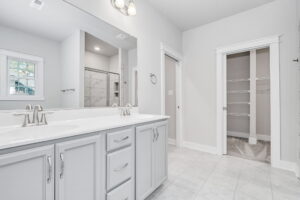 A modern bathroom featuring a double vanity, tiled shower, and a walk-in closet with shelving.