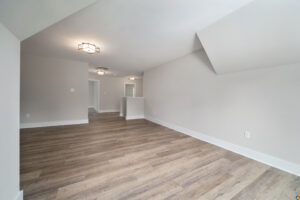 Empty room with wooden flooring, white walls, and contemporary light fixtures. The space features a small partition wall and an angled ceiling.