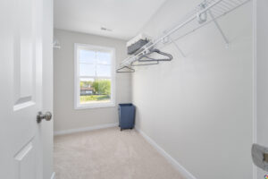 Empty walk-in closet with beige carpeting, white walls, wire shelving, a window, and a blue laundry basket.
