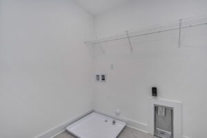 Empty laundry room with a white wire shelf, washer and dryer hookups, a designated area for appliances, and a small pet door on the right side.