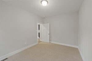 Empty room with beige carpet, light gray walls, a white ceiling light fixture, and a partially open white door leading to another room.