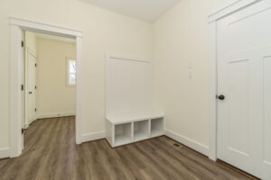 An empty room with beige walls, a white bench with storage cubbies, and two closed doors leading to other rooms.