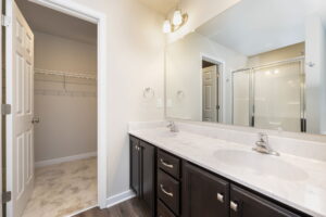 Modern bathroom with double sink vanity, large mirror, and view into a walk-in closet with wire shelving.