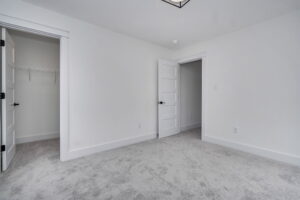 A clean, empty room with white walls, gray carpet, a closet with an open door on the left, and another open door on the right.