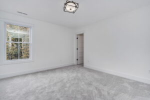 Empty room with light gray carpet, white walls, a single window on the left, and a door adjacent to the window. Ceiling has a geometric black light fixture.