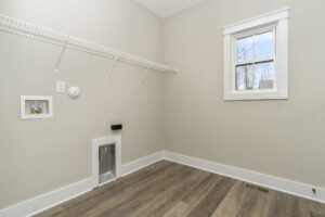 A small, empty room with a window, gray walls, a white door with a built-in pet entrance, and a wall-mounted wire shelf.