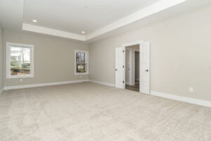 Empty living room with beige carpet, white walls, multiple windows, and open white doors.