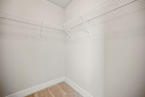 Empty walk-in closet with beige carpet, white walls, and white wire shelving units mounted on two sides.