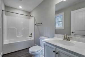 A modern bathroom with a white bathtub and shower combo, a toilet, and a sink with a marble countertop; the room also has a mirror above the sink and a small window.