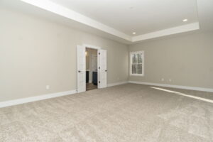 Empty living room with beige carpet, gray walls, recessed lighting, and two doors, one open revealing another room.
