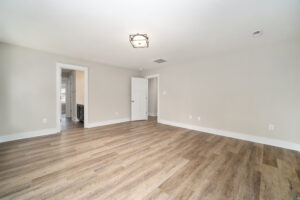 Spacious empty room with light-colored walls, hardwood floors, and a modern ceiling light fixture. The room has doorways leading to other areas of the house.