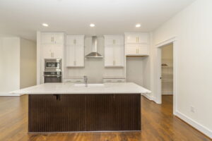 Modern kitchen with white cabinetry, a large island with a dark base, built-in appliances, and hardwood floors.