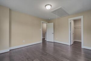An empty room with beige walls, dark hardwood floors, a closed door on the left, an open door on the right leading to a closet, and a ceiling light fixture.