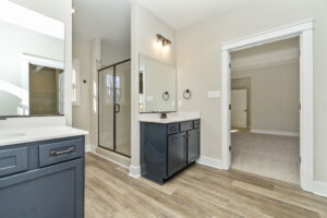 Modern bathroom with a dark blue vanity, white walls, and glass shower doors next to a carpeted bedroom entrance.