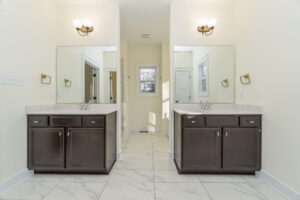 A bright, symmetrical bathroom with two dark wooden vanities, marble floors, mirrors, and wall-mounted lights.