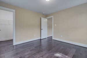 An empty room with beige walls, dark hardwood flooring, and a white door leading to a closet with wire shelving. Door is partially open, revealing additional space beyond.