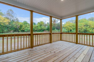 Wooden porch with railings and roof, overlooking a grassy yard and dense trees.
