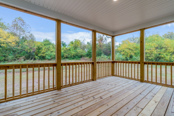 Wooden porch with railings and roof, overlooking a grassy yard and dense trees.