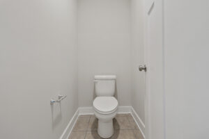 A small bathroom with a white toilet, empty toilet paper holder, gray tiled floor, and white walls.