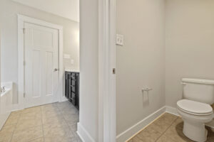 A bathroom with a toilet, a black vanity with a sink, a white door, beige tiled floor, and light gray walls.