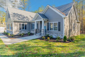 A modern single-story house with gray siding, stone accents, and a well-manicured front lawn under a clear blue sky.