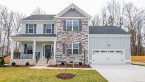Two-story house with stone facade, porch, and attached garage surrounded by trees and lawn.
