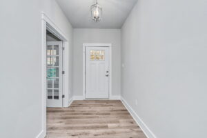 Empty hallway in a modern home with gray walls, wooden floors, a white door at the end, and a glass-paneled door on the left.