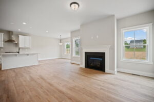 A spacious, unfurnished open-concept living area with a modern kitchen, a fireplace, large windows, and hardwood flooring.