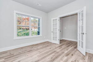 Empty modern room with hardwood floors, a large window displaying fall foliage, and an open french door.