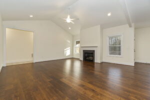 Spacious living room with hardwood floors, white walls, a fireplace, and multiple windows allowing natural light.