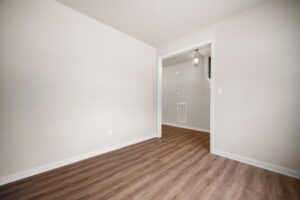 Empty room with wooden flooring, white walls, and an open doorway leading to another room with a hanging light fixture.
