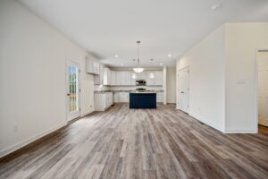Spacious, modern kitchen with white cabinets, a center island, stainless steel appliances, pendant lights, and light wood flooring. Door and windows provide natural light.