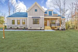 A modern beige house with a dark roof sits elegantly amid the highland landscape, surrounded by lush trees and a vibrant grass yard.