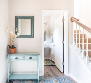 Bright hallway with a light blue console table, a potted orchid, and a mirror. an open door leads to a bathroom, with a staircase on the right.