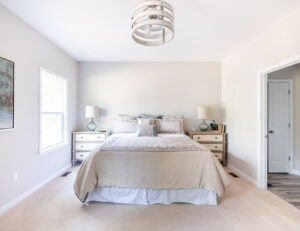 Bright, minimalist bedroom with a large bed, two side tables with lamps, a dresser, and a modern ceiling light fixture.