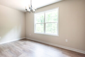 An empty room with light wood flooring, beige walls, a large window, and a ceiling light fixture.
