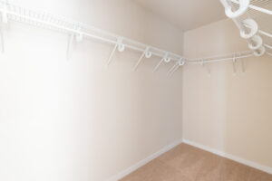 An empty walk-in closet with beige walls, carpeted floor, and white wire shelving and hanging rods along the walls.