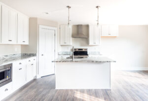 Modern kitchen interior with white cabinetry, stainless steel appliances, and a center island under pendant lights.