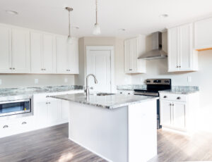 Modern kitchen interior with white cabinets, granite countertops, and stainless steel appliances, including a built-in oven and electric stove.