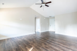Empty modern living room with hardwood floors, white walls, and a ceiling fan.